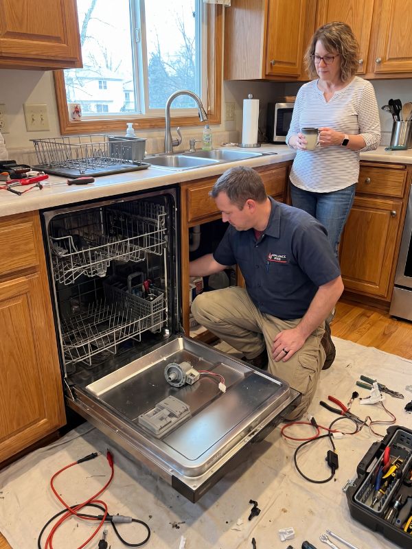 Appliance repair technician servicing a built-in dishwasher for drainage, leak, and spray-arm problems in a Lubbock, TX kitchen